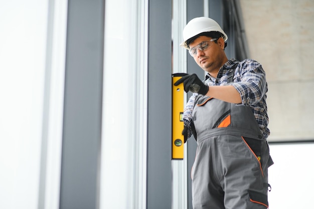 Workman in overalls installing or adjusting plastic windows