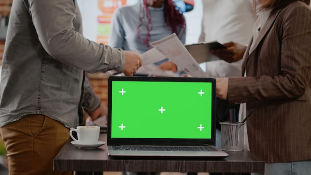 写真 スタートアップオフィスのラップトップで緑色の画面を使用し、分離されたモックアップテンプレートとクロマキーディスプレイの背景を使用して、論文を扱う同僚。コピースペースでビジネスに取り組んでいる同僚。
