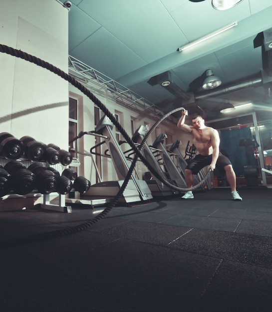 Workout concept. Powerful attractive young man workout with ropes at gym.