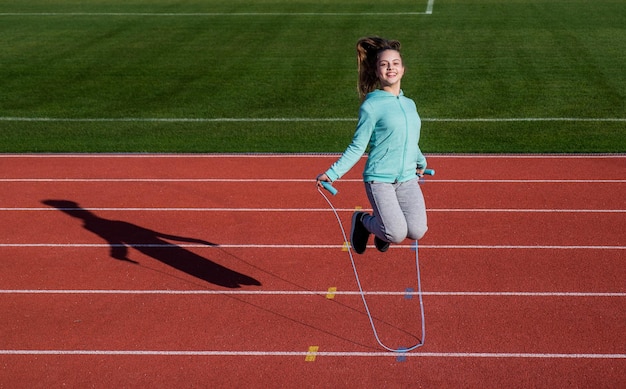 A workout routine kid in sportswear jump on skipping rope child do exercise on racing track healthy childhood workout on fresh air outdoor jumping rope teen girl warming up on stadium