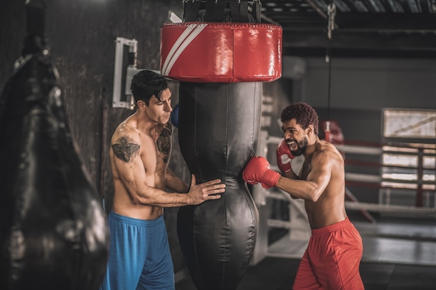 Workout. Two men exercising in a gym and kicking the sandbag