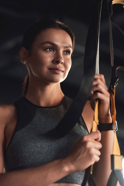 Foto allenamento. colpo verticale di una giovane donna attraente che tiene cinturini fitness trx mentre si allena in palestra industriale. sport, benessere e stile di vita sano