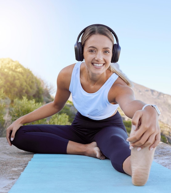 Allenamento yoga stretch cuffie streaming musica e donna all'aperto su un tappetino ritratto di un sorriso felice da esercizio benessere femminile e stretching sano prima dell'allenamento in natura su una montagna