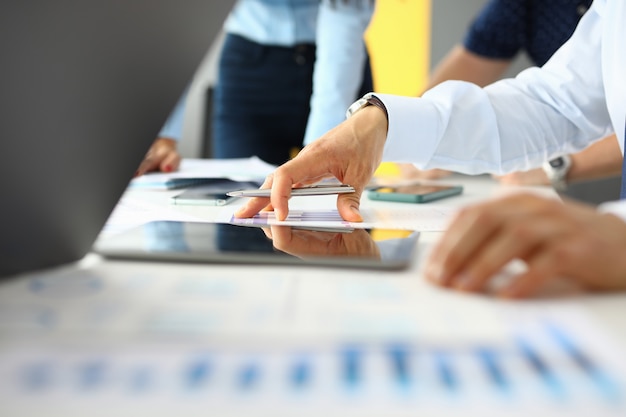 Workplace in business office on table are tablet documents co-workers hold pens in their hands.