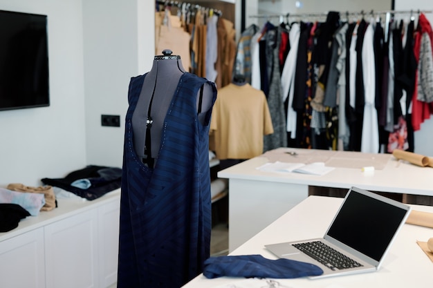 workplace of contemporary seamstress or tailor with unfinished clothing item on mannequin, laptop and piece of textile on desk