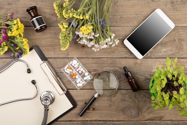 Workplace of a doctor Stethoscope clipboard pills smartphone and other stuff on wooden desk