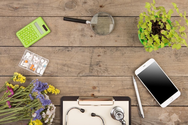 Workplace of a doctor Stethoscope clipboard pills smartphone and other stuff on wooden desk