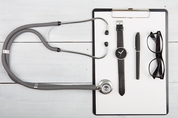 Workplace of doctor stethoscope medicine clipboard glasses and watches on wooden desk