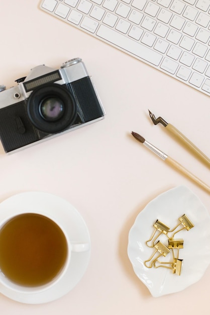 Workplace of a female photographer or calligrapher Keyboard camera caligraphy pens paper clips and a cup of tea lie on a beige background