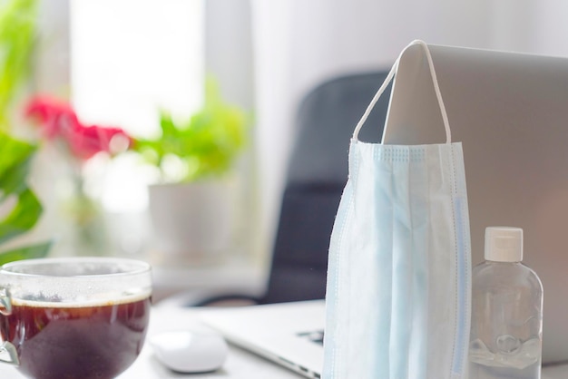 Workplace at home by the window with a laptop protective face mask and sanitizer concept of quarantine during coronavirus pandemic in the world