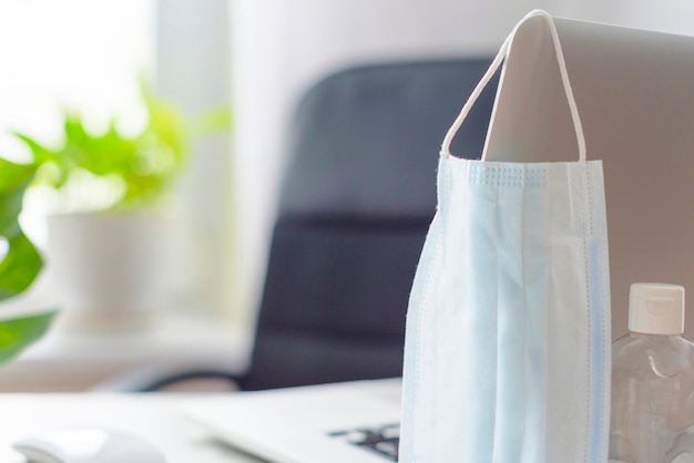 Luogo di lavoro a casa vicino alla finestra con una maschera protettiva per laptop e un concetto di disinfettante di quarantena durante la pandemia di coronavirus nel mondo