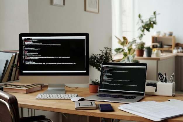 Workplace of IT programmer with desktop computer and laptop with coded data on their screens