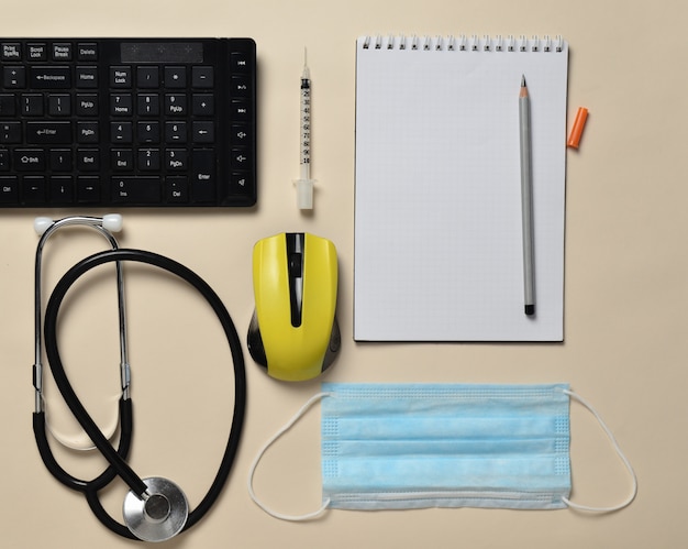 Workplace of a modern doctor. Keyboard, wireless mouse, notebook, stethoscope, syringe on pastel background, top view, minimalist trend