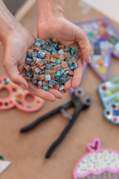 Photo workplace of the mosaic master: women's hands holding mosaic details in the process of making a mosaic