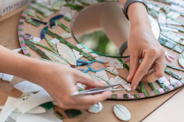 Photo workplace of the mosaic master womens hands holding tool for mosaic details in the process of making...