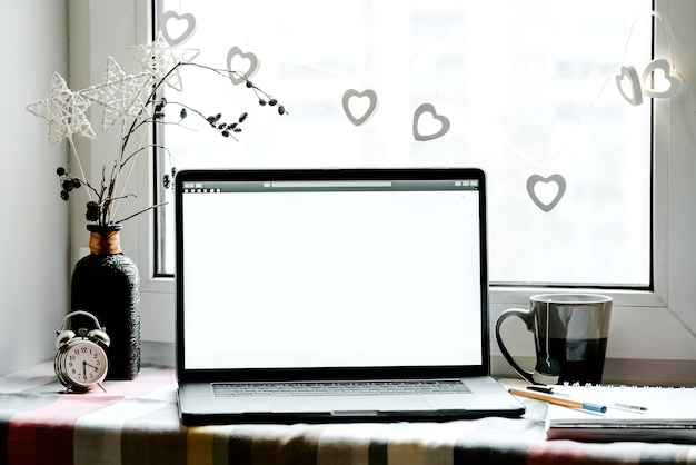 Workplace near the window with white laptop screen standing on windowsill