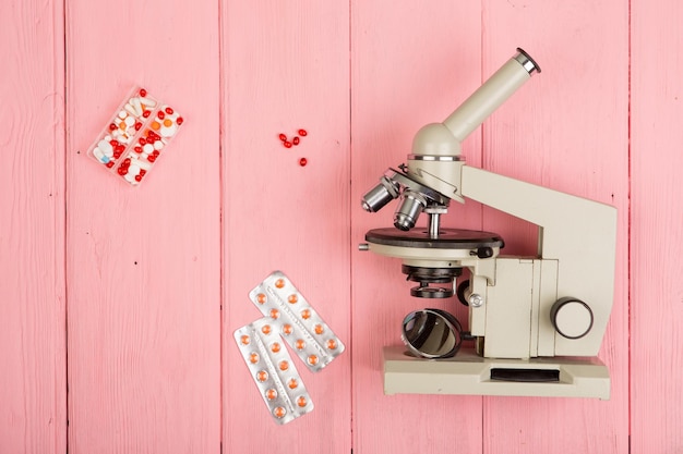 Таблетки микроскопа врача ученого рабочего места на розовом деревянном столе