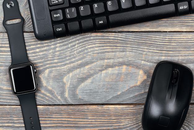 Workplace smart watch, keyboard, mouse on a wooden table.