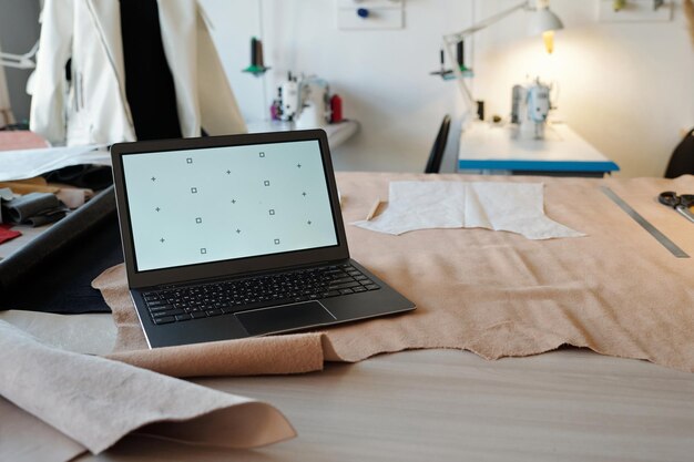 Workplace of tanner or taillor with laptop standing on beige textile