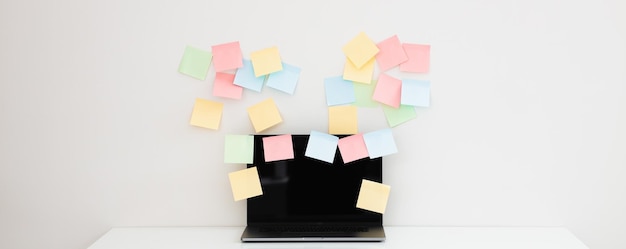 Workplace with blank sticky notes and modern laptop near white wall