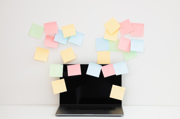 Workplace with blank sticky notes and modern laptop near white wall