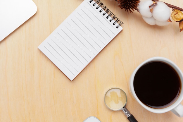 Workplace with coffee, spiral notebook and magnifying glass