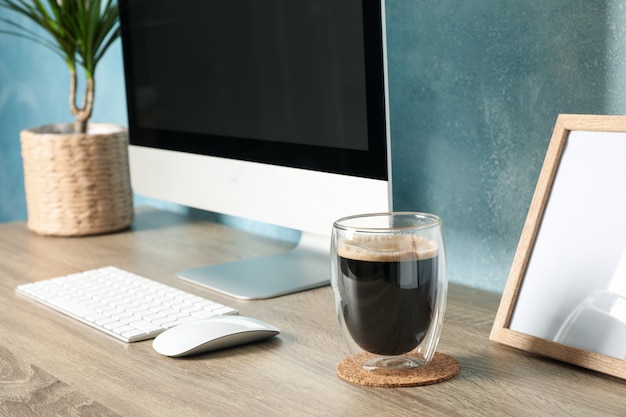 Workplace with computer and plant on wooden table. Blue