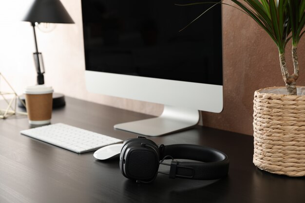 Workplace with computer and plant on wooden table. Light brown