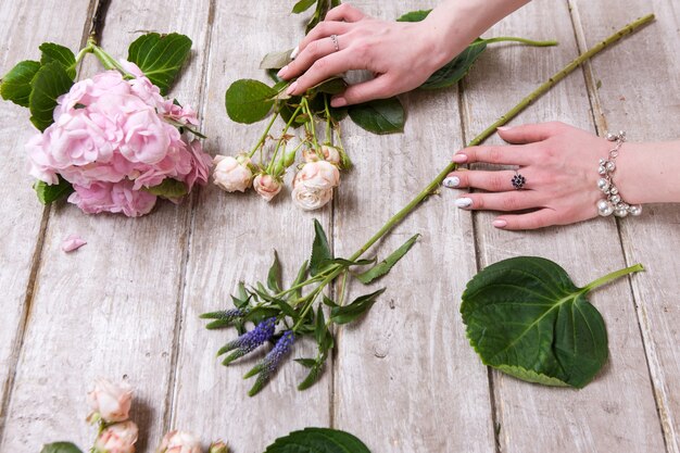 花のある職場。花屋の手。フローリストリーワークショップ木製テーブルの背景。春の花からの装飾アートワーク