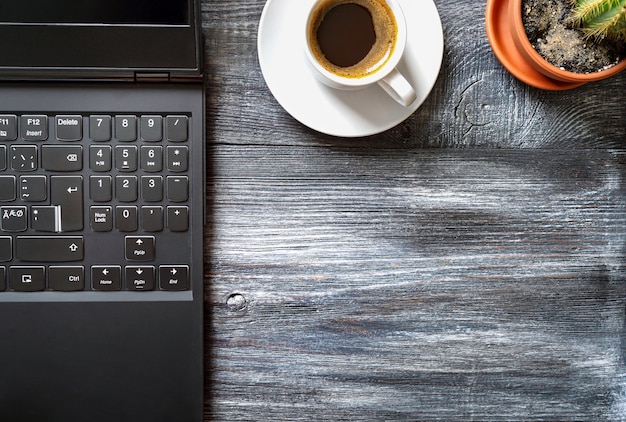 Posto di lavoro con laptop, tazza di caffè, cactus su un tavolo di legno, vista dall'alto, piatto con spazio per le copie. lavoro a casa. formazione in linea.