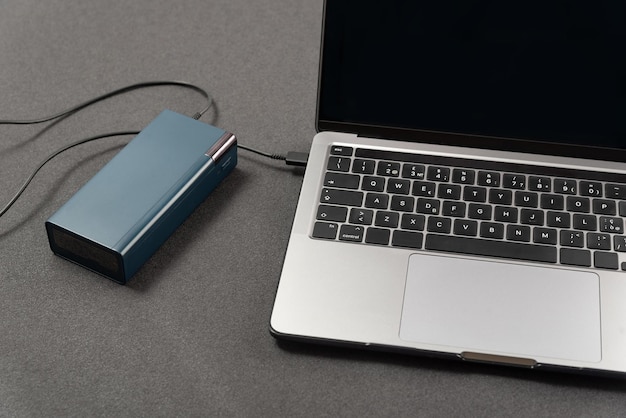 Photo workplace with laptop is charged by power bank laptop is connected by cord to an external battery