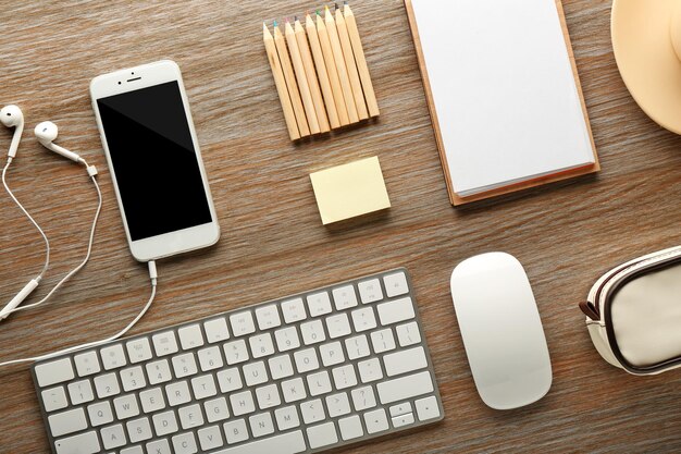 Workplace with mobile phone peripheral devices and stationery on wooden table