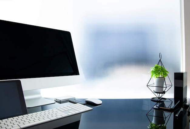 Workplace with modern computer on glass table, Mock up black screen, Houseplant and supplies.