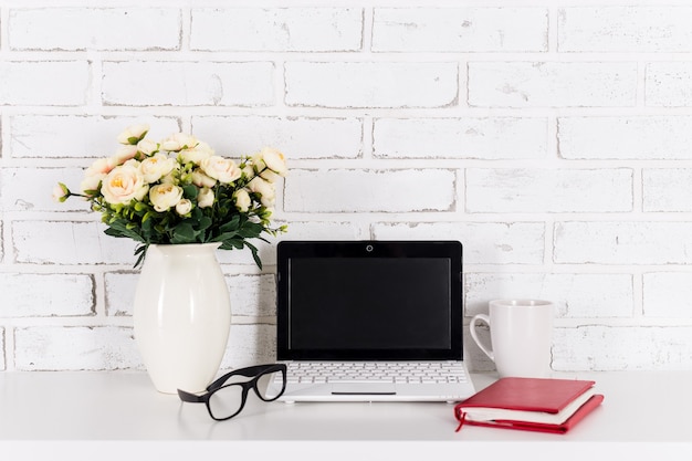 Workplace with modern laptop over white brick wall background