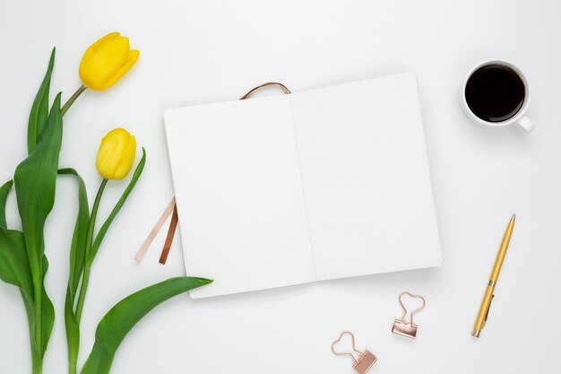 Workplace with white notebook stationery coffee cup and yellow tulips on white desk Flat lay office desk mock up space for text Top view Copy space