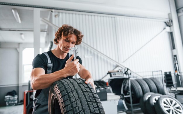 Works with tire Adult man in grey colored uniform is in the automobile salon