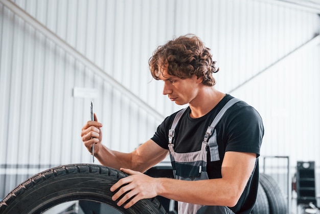 タイヤで動作します灰色の制服を着た大人の男性が自動車サロンにいます