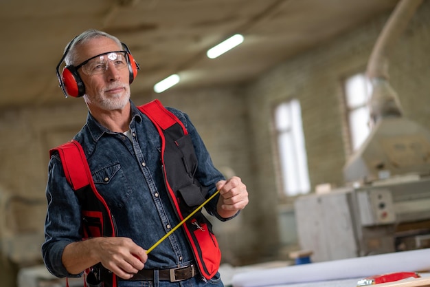 Photo in a workshop. man in ear protectors and measuring tape in hands