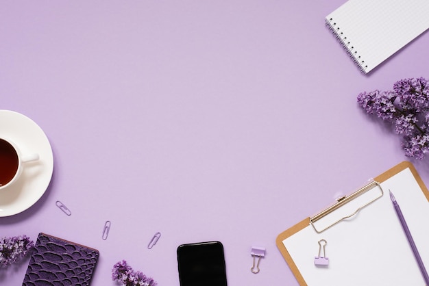 The workspace of a blogger or freelancer Flat lay with a cup of coffee notebooks and lilac branches stationery on a lilac background with a copy space