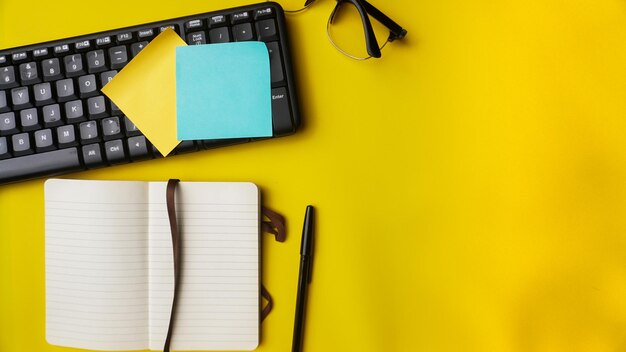 workspace desk with notebooks pens keyboard glasses plants and coffee on blue background