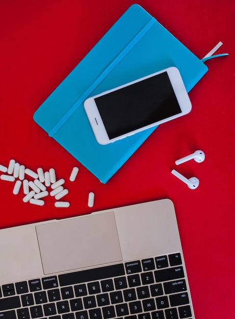 Фото Рабочее пространство ноутбук мобильный телефон и блокнот с рассеянными планшетами почти верхний вид красный фон
