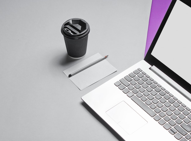 Workspace minimal concept. Notebook, sheet of paper with a pencil, cardboard container of coffee on purple gray table