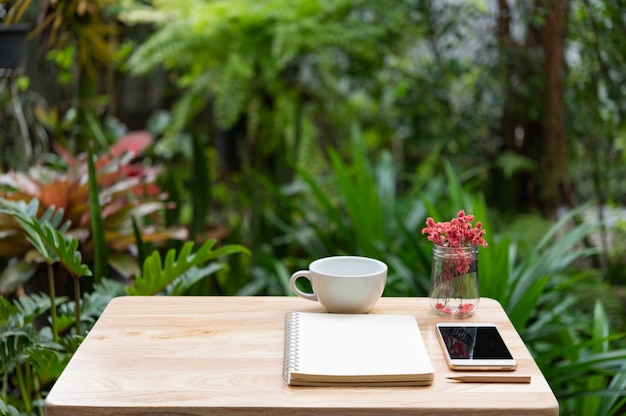 Workspace outdoors with memo notebook, pencil, white coffee cup, mobile phone 