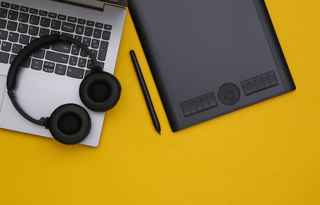 Workspace of retoucher or graphic designer. Laptop, graphic tablet and headphones on yellow background. Top view.