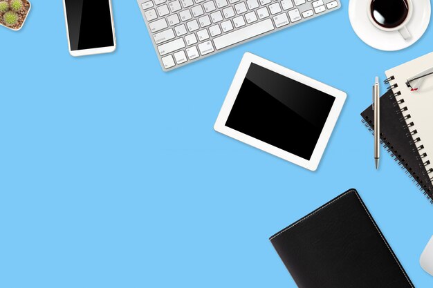 Workspace table with laptop computer, office supplies, coffee cup, cell phone and coffee cup on blue pastel