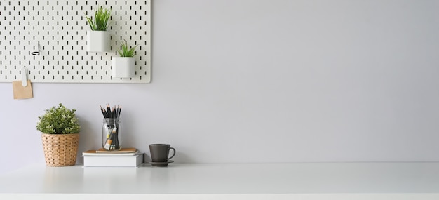 Workspace that surrounded by coffee cup, diary, notebook, book, pencil holder, plant in wicker basket and potted plant. Orderly workplace concept.