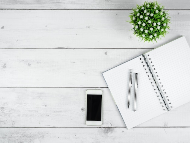 Workspace on white wood table top view copy spaceSilver pen on blank page notebook and smartphone