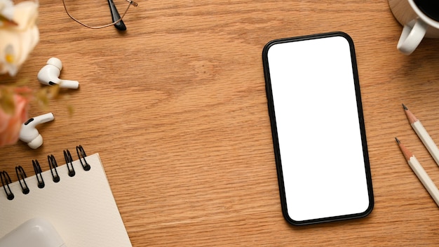 Workspace with cellphone mockup pencils spiral notepad earbuds and copy space on wood background