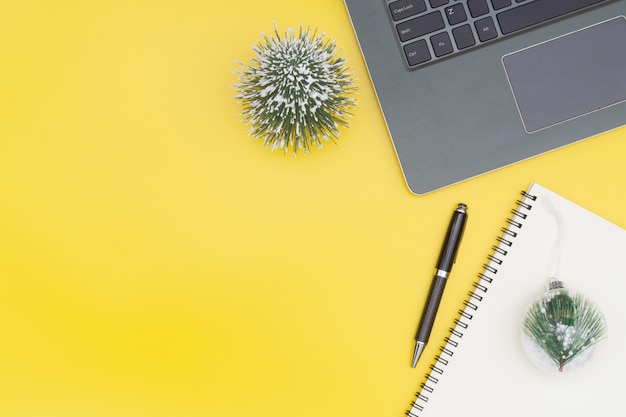 Workspace with Christmas decoration and notebook, top view yellow background