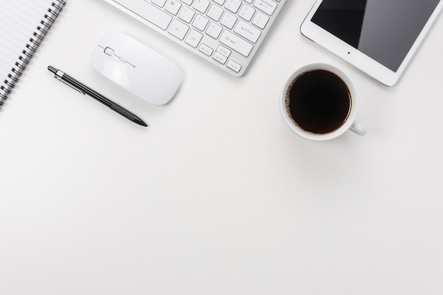 Workspace with computer keyboard, office supplies, and coffee cup on white background.